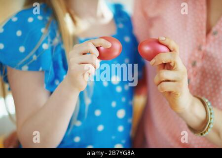 Closeup on mother and daughter having egg tapping with red easter eggs at home in sunny spring day. Stock Photo