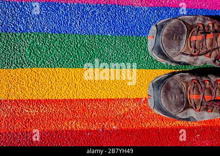 A man steps on his boots with the gay flag, painted on the ground, a concept of contempt for rights. Stock Photo