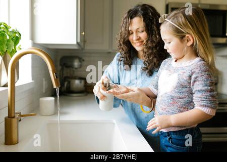 Mother and daughter washing hands in kitchen sink Stock Photo
