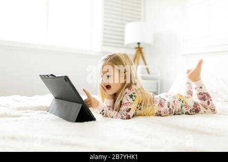 Girl in pajamas using digital tablet while lying on bed Stock Photo