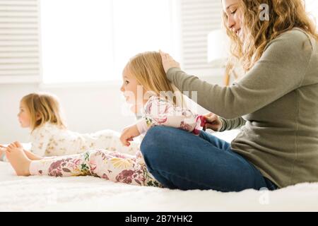 Woman brushing her daughter's hair on bed Stock Photo