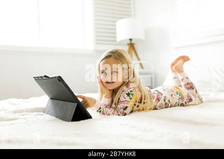 Girl in pajamas using digital tablet while lying on bed Stock Photo