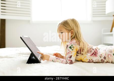 Girl in pajamas using digital tablet while lying on bed Stock Photo