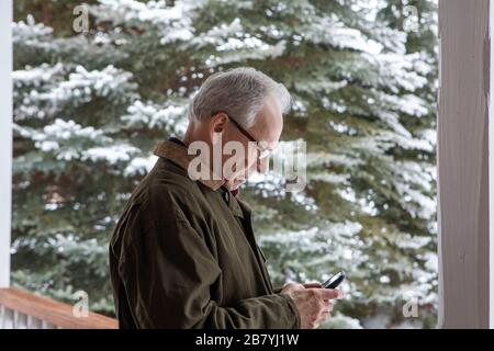 Senior man using smart phone by snowy tree Stock Photo