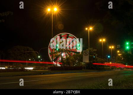 Long exposure of colorful ferris wheel and light trails on the expressway road at night. Time exposure of traffic lights on avenue in Florianopolis. C Stock Photo