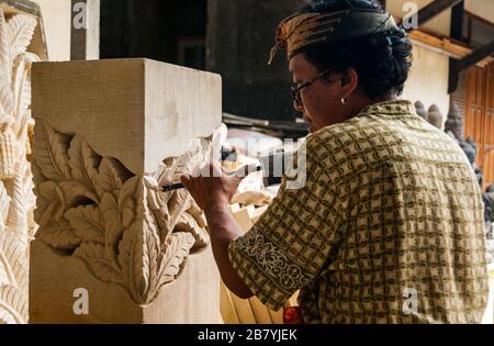 A Balinese artisan hard at work sculpting a statue out of a block of stone using a hammer and chisel. Stock Photo