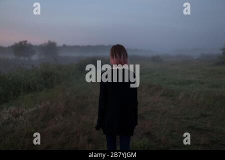 Rear view of young woman in field at sunset Stock Photo