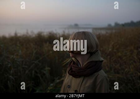 Young woman in field by lake at sunset Stock Photo