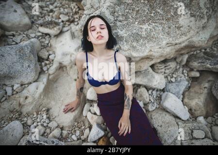 Tattooed woman in blue bra sitting on rocks Stock Photo