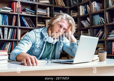 Unhappy bored male student studying looking at laptop. Stock Photo
