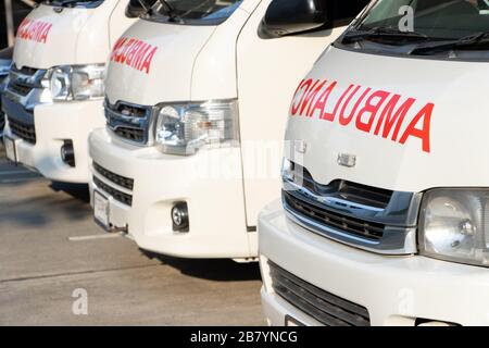 Front part of ambulances standing in parking lot of hospital. A row cars of rescuers with red text ambulance on hood. Stock Photo