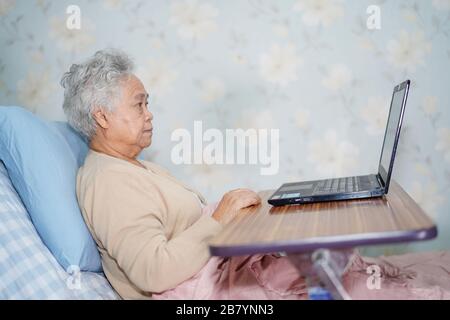 Asian senior or elderly old lady woman patient using notebook computer and smile with doctor while sitting on bed in nursing hospital ward : healthy s Stock Photo