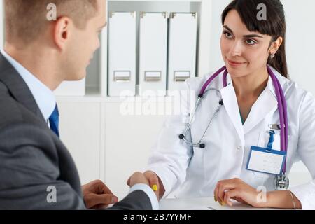Beautiful smiling female medicine doctor shaking hands with male patient Stock Photo