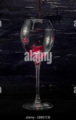 Red wine in a glass on a black background. Pouring wine. Stock Photo