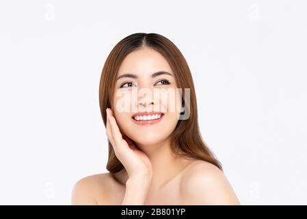 Cheerful beautiful smiling Asian woman with clear fair skin doing hand touching face pose while looking up in white isolated background Stock Photo