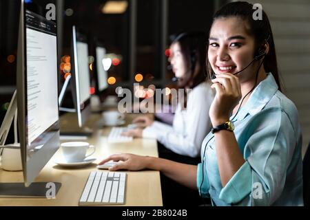Asian young adult confidence operator colleague team with headsets working in a call center at night as customer service and technical support. Using Stock Photo