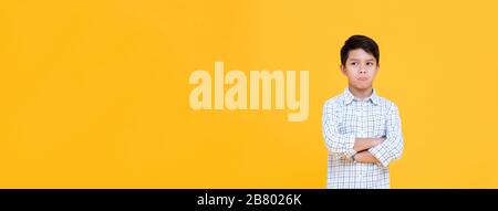Sulky bored boy pouting mouth and thinking with arm crossed gesture isolated yellow banner background Stock Photo