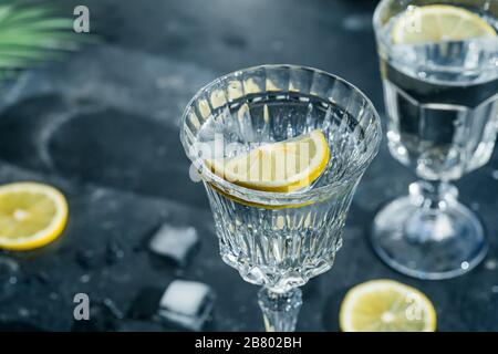 Water lemon detox. Pure cold water with lemon in crystal glasses on a dark background in the sunny summer sun. Stock Photo