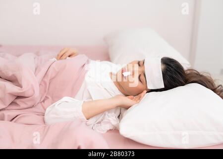 Flu. Closeup image of frustrated sick woman with red nose lying in bed in thick scarf Stock Photo