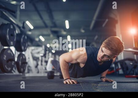 Young athletic man doing push-ups in gym. Muscular and strong guy exercising Stock Photo