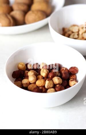 Various Sorts of Nuts on the Table. Hazelnuts, Walnuts and Cashew Nuts in Bowls on White. Stock Photo