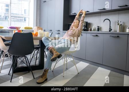 Young woman sitting at the kitchen table, stretching Stock Photo
