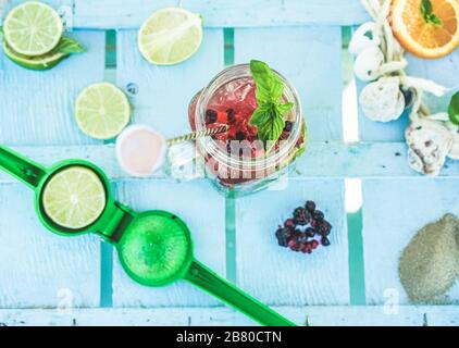 Top view of berries mojito on blue wood bar counter with lime squeezer and tropical fruit ingredients - Summer, cocktails, drinks, party and concept - Stock Photo
