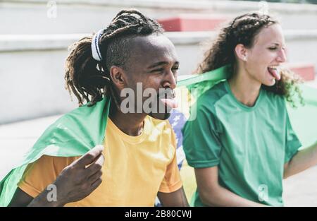 Two brazilian sport fans celebrating their country - Multiracial supporters having fun at stadium for olympic games - Vintage desaturated retro filter Stock Photo