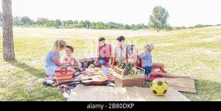 Happy families making picnic in city park - Young parents having fun with their children in summer time eating, laughing and playing together - Love a Stock Photo