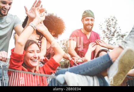 Young millennials people racing with shopping cart - Happy crazy friends having fun with trolleys in car park - Youth lifestyle and party concept - Fo Stock Photo