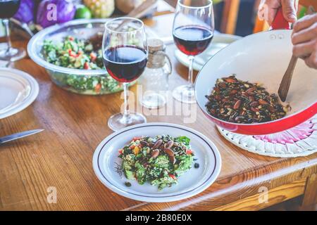 Male chef serving organic vegan salad for dinner - Cook man preparing the table for meal with vegetarian food and ecologic wine - Focus on dish salad Stock Photo