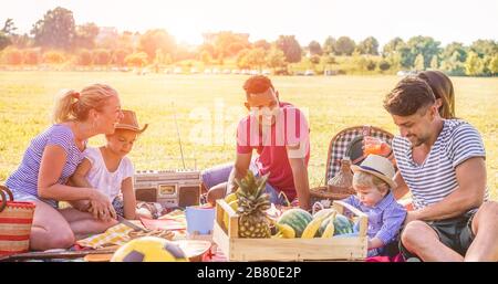 Happy families doing picnic in nature park outdoor - Young parents having fun with children in summer time eating and laughing together - Positive moo Stock Photo