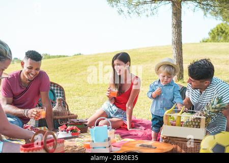 Multiracial happy families doing picnic in park outdoor - Young parents having fun with children in summer time eating together - Food, weekend lifest Stock Photo