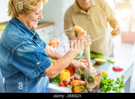 Senior couple cooking healthy vegetarian meal with fruits and vegetables together - Old happy people taking care about diet and health - Vegan and bio Stock Photo