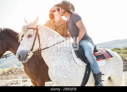 Couple kissing and riding horses during sunny day - Happy lovers having fun on summer vacation - Love between people , nature and holiday concept - Ma Stock Photo