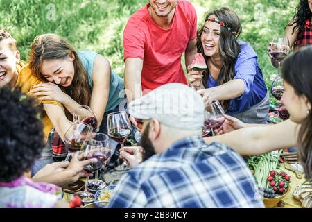 Group of happy friends cheering with glasses of red wine and eating fruits and vegetables - Young people having fun on city park  - Focus on right hip Stock Photo