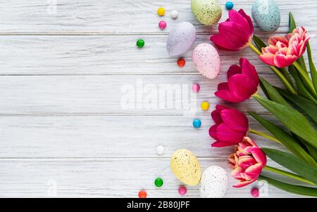 Easter composition with colorful  eggs, tulips and chocolate candy on white wooden background, space for text. Top view, flat lay. Stock Photo