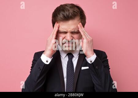 Worried young man in suit suffering from headache. studio shot on pink wall. Stock Photo