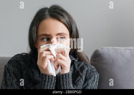 Sad sick young woman with handkerchief. Female with cough, snot, fever sitting at home on sofa, copy space Stock Photo