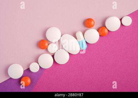 Pills and tablets in diagonal row on bright pink, violet and purple background, healthcare medical concept, antibiotics and cure, top view Stock Photo