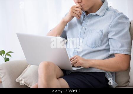 Happy young Chinese man using laptop in living room Stock Photo