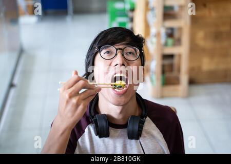 Asian guy with helmets and glasses eating Asian food with sticks in a restaurant Stock Photo