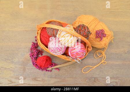 Wicker basket with knitting needles and a knitting on wooden table in garden. Stock Photo