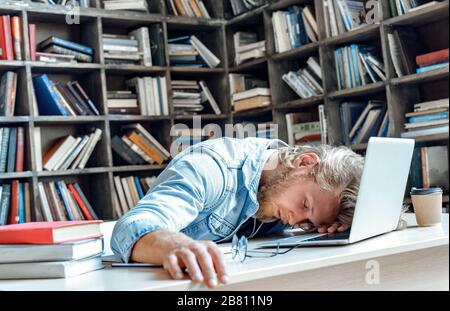Funny tired sleepy university student sleeping sitting at library desk. Stock Photo