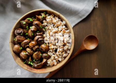 Sauteed whole white mushrooms with buckwheat in wooden bowl on table Stock Photo