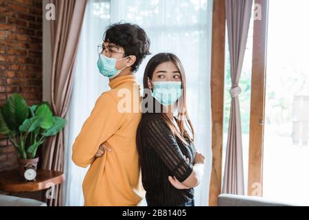 man and woman standing back to back wearing face masks while sick Stock Photo