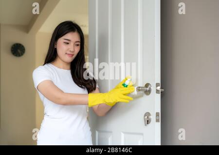 Normal shot of a Asian woman disinfecting the door knobs by spraying a blue sanitizer from a bottle. Prevent the virus and bacterias, Prevent covid19, Stock Photo