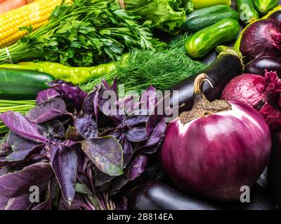 tabletop arrangement of a variety of fresh fruits and vegetables sorted by colors - pepper, tomato, corn, carrot, green salad, cilantro, eggplant. Stock Photo