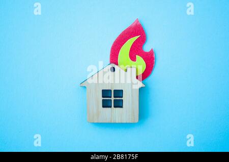 Fire house, insurance and mortgage concept. Small wooden house toy and paper fire shape on blue background top view Stock Photo