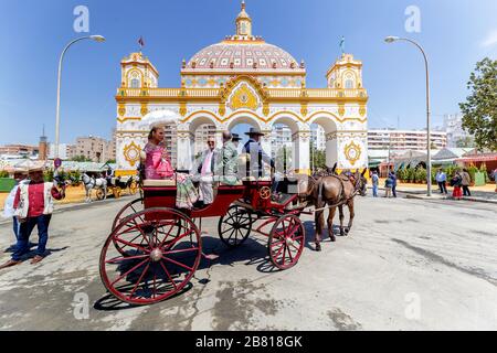 Woman with umbrella in traditional dress travelling in a horse drawn carriage at the April Fair (Feria de Abril), Stock Photo